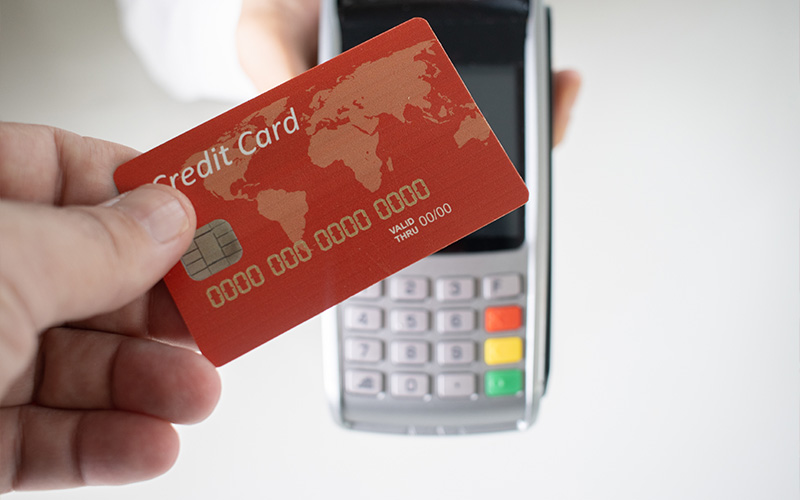 A person handing over a red credit card to be swiped at a payment terminal